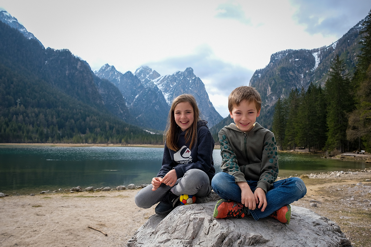due bambini su un sasso con il lago di Dobbiaco sullo sfondo